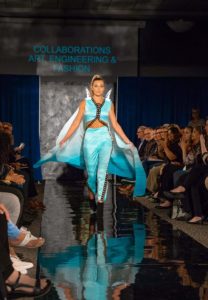 A model with a flowing cape walks down the fashion runway!