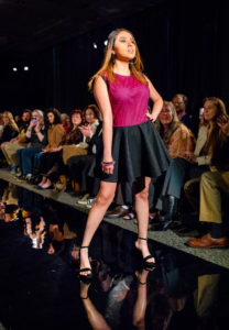 A model poses at the end of the fashion runway as the crowd looks on. 