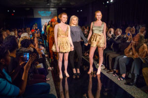 Student designer poses at the end of the fashion runway with her two models. 
