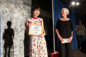 Patricia Bowers the winner of the "Karinas Dress Challenge" hold her award and smiles as Professor Kristen Flynn looks at her smiling. 