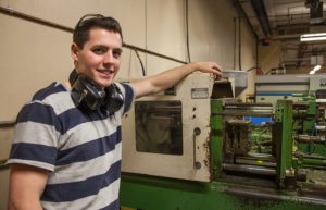 Engineering student stands smiling near large machine. 