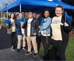 Five students standing with cheerleader pom-poms smiling. 