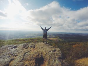 Young man standing on top of a mountain hands up in the air. 