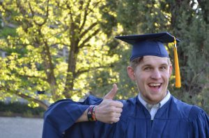 Man in blue cap and gown with thumbs up