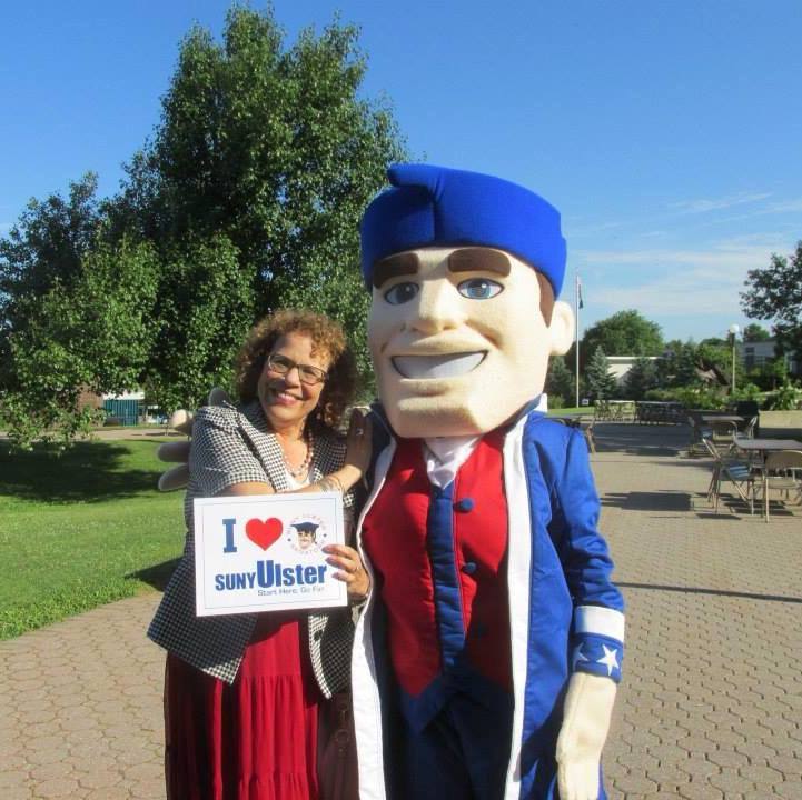 Mindy Kole standing with Senator Sam mascot and holding an "I love SUNY Ulster sign"