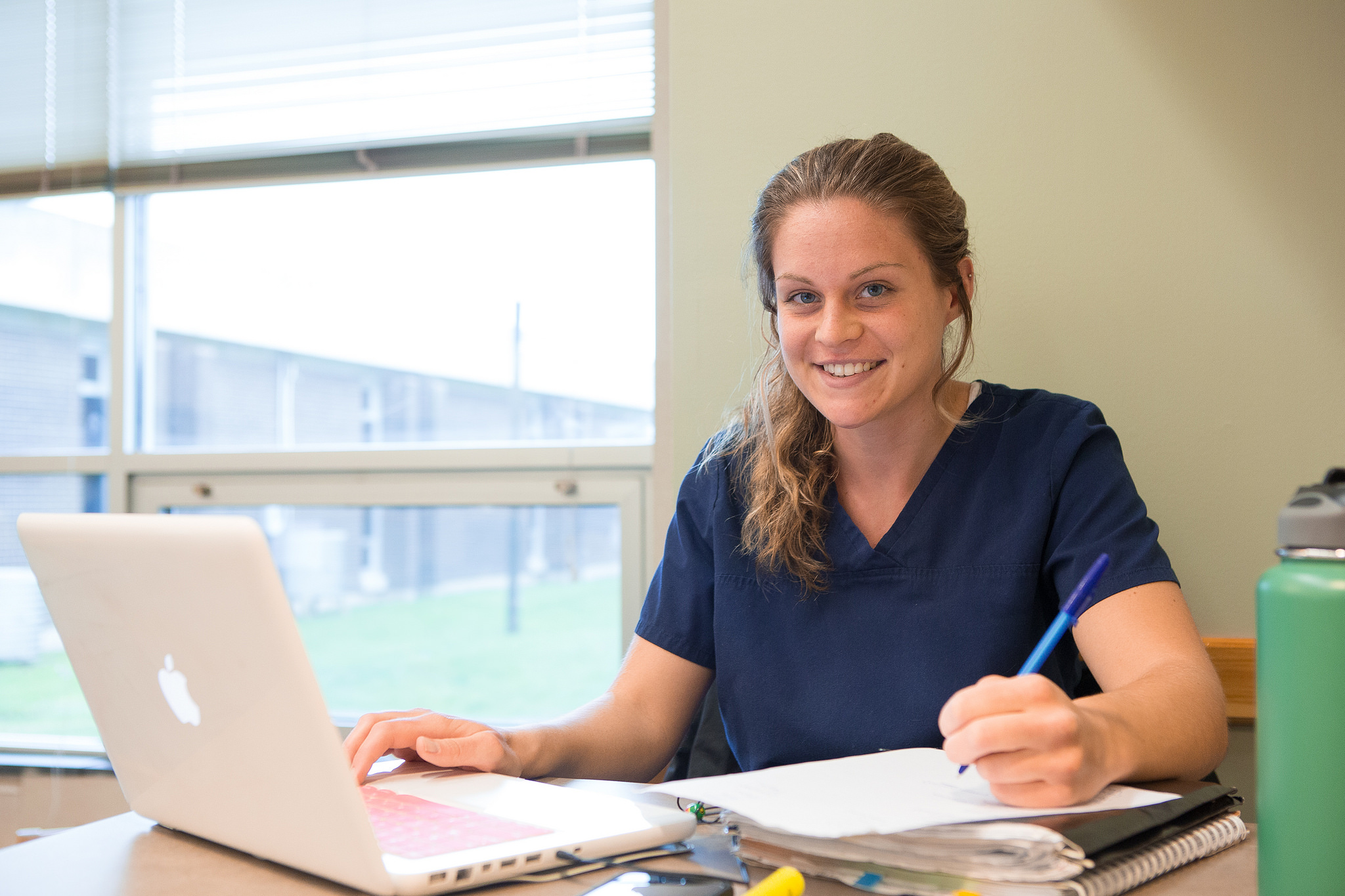 Girl Working at Laptop in Library Smiling at Camera While Doing Homework