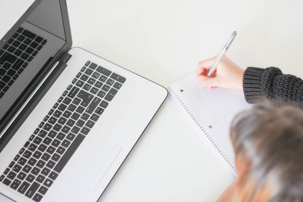Woman writing in notebook and looking at laptop