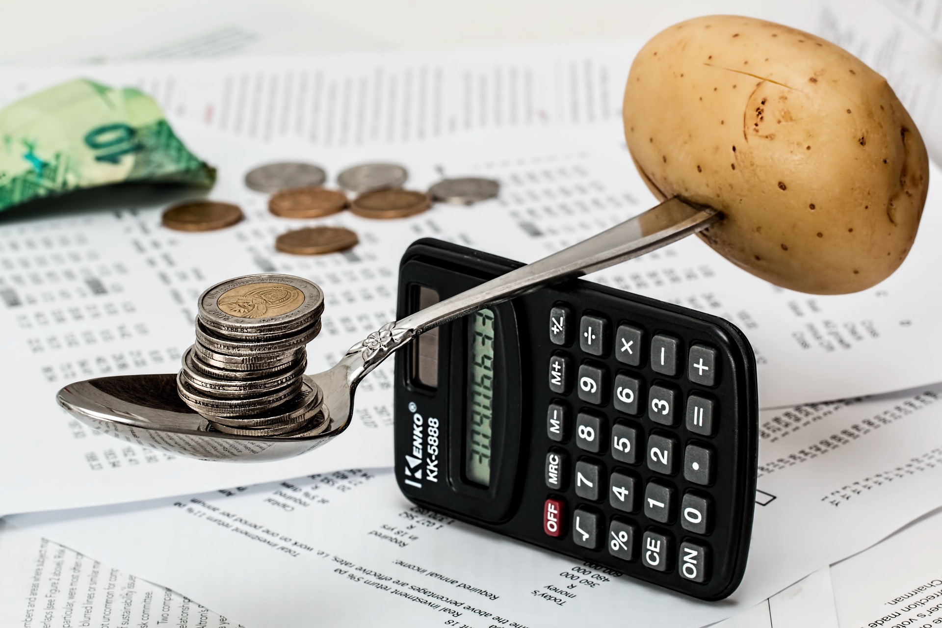 Spoon holding potato on one end and money in the other while balanced on a calculator