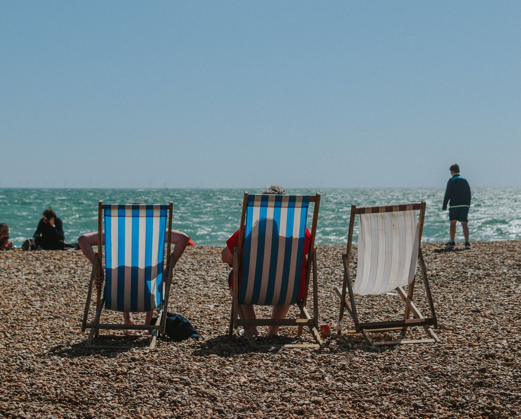 Three lawn chairs in a row on a beach with the ocean in the distance.