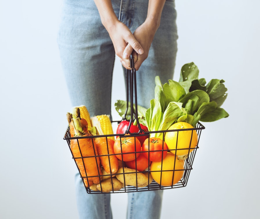 person holding shopping basket full of vegetables