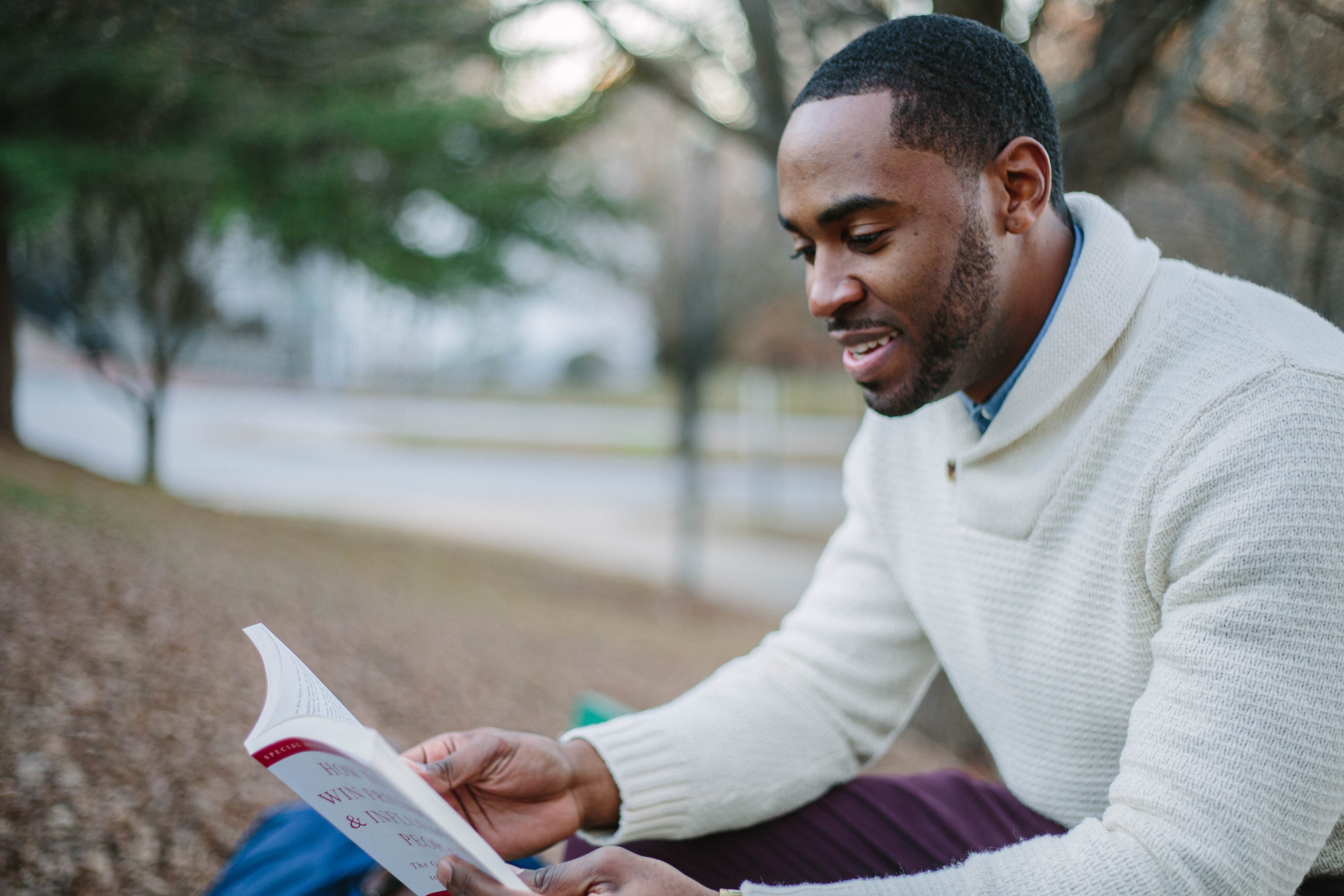 a man sits outside in a warm sweater, happily reading a self-help book