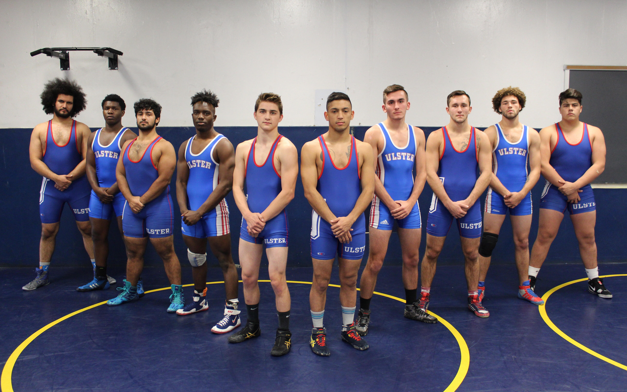 ten diverse SUNY Ulster male wrestling team members stand posed uniformly in their singlets with hands crossed in front of them