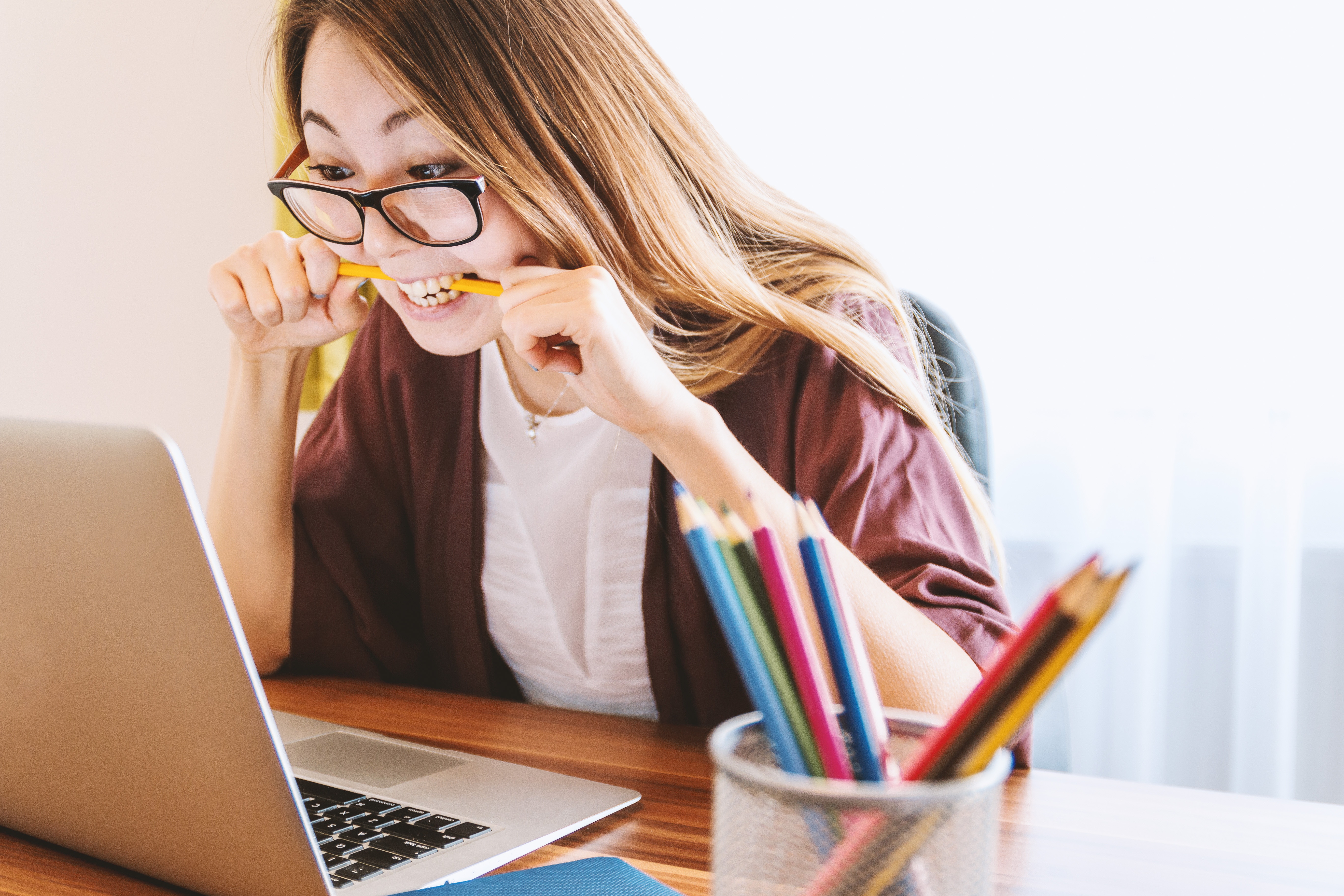 A woman sits at a desk biting a pencil as she looks at a computer screen
