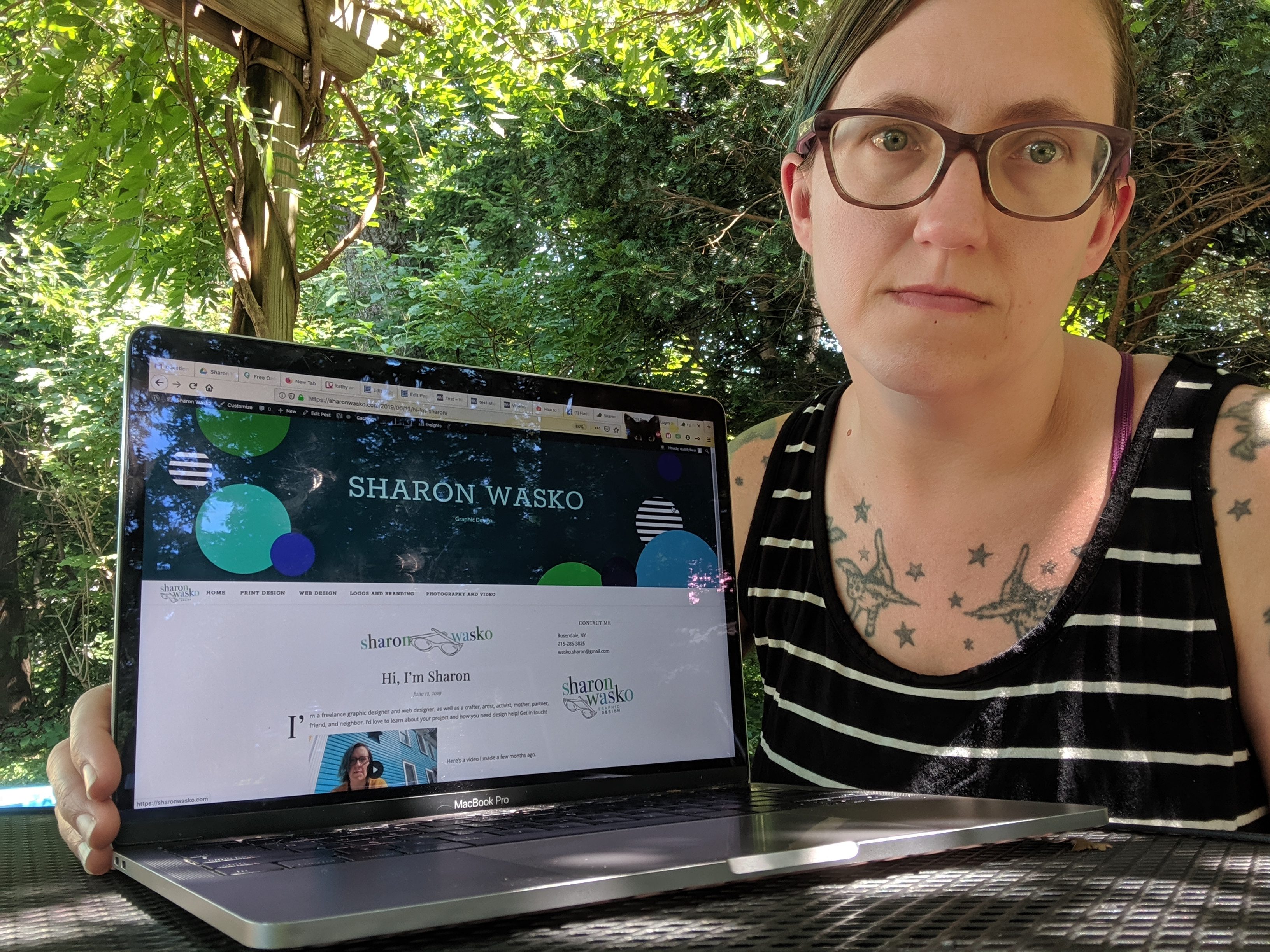 Sharon sitting at an outdoor picnic table with an open laptop that displays her website on the screen.
