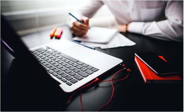 A person sits at a desk with a laptop, two books and a cell phone on the table